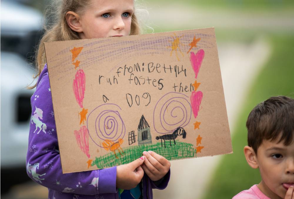 Young girl from the GVSU Children's Enrichment Center holding a handmade sign that reads "Run faster than a dog"